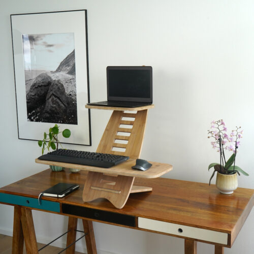 Gaia Craft Hæve sænkebord i bambus 'Naturlig' med en bærbarcomputer, et tastatur og computermus på. Hæve sænkebordet står på et dekoreret skrivebord