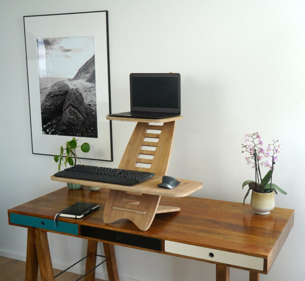 Gaia Craft Hæve sænkebord i bambus 'Naturlig' med en bærbarcomputer, et tastatur og computermus på. Hæve sænkebordet står på et dekoreret skrivebord